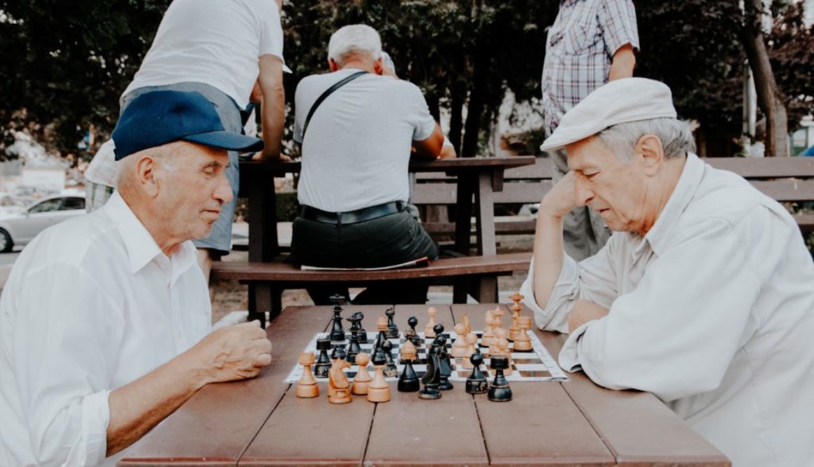 men playing chess on a table in the park thinking hard about their next move