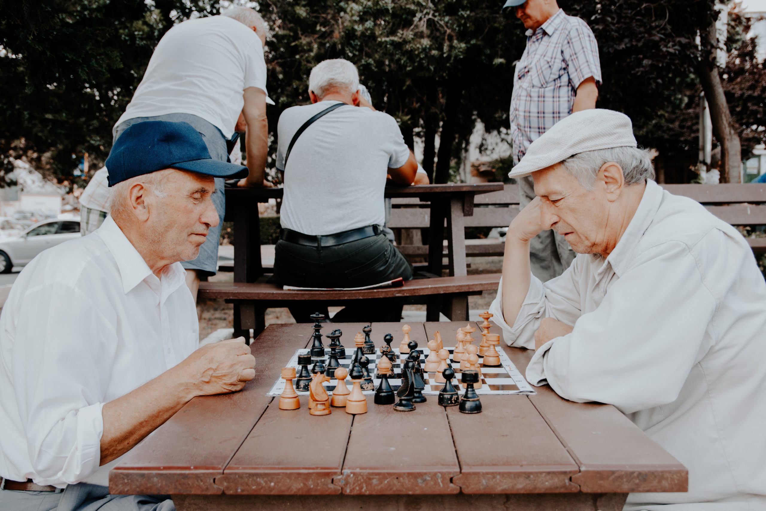 men playing chess on a table in the park thinking hard about their next move